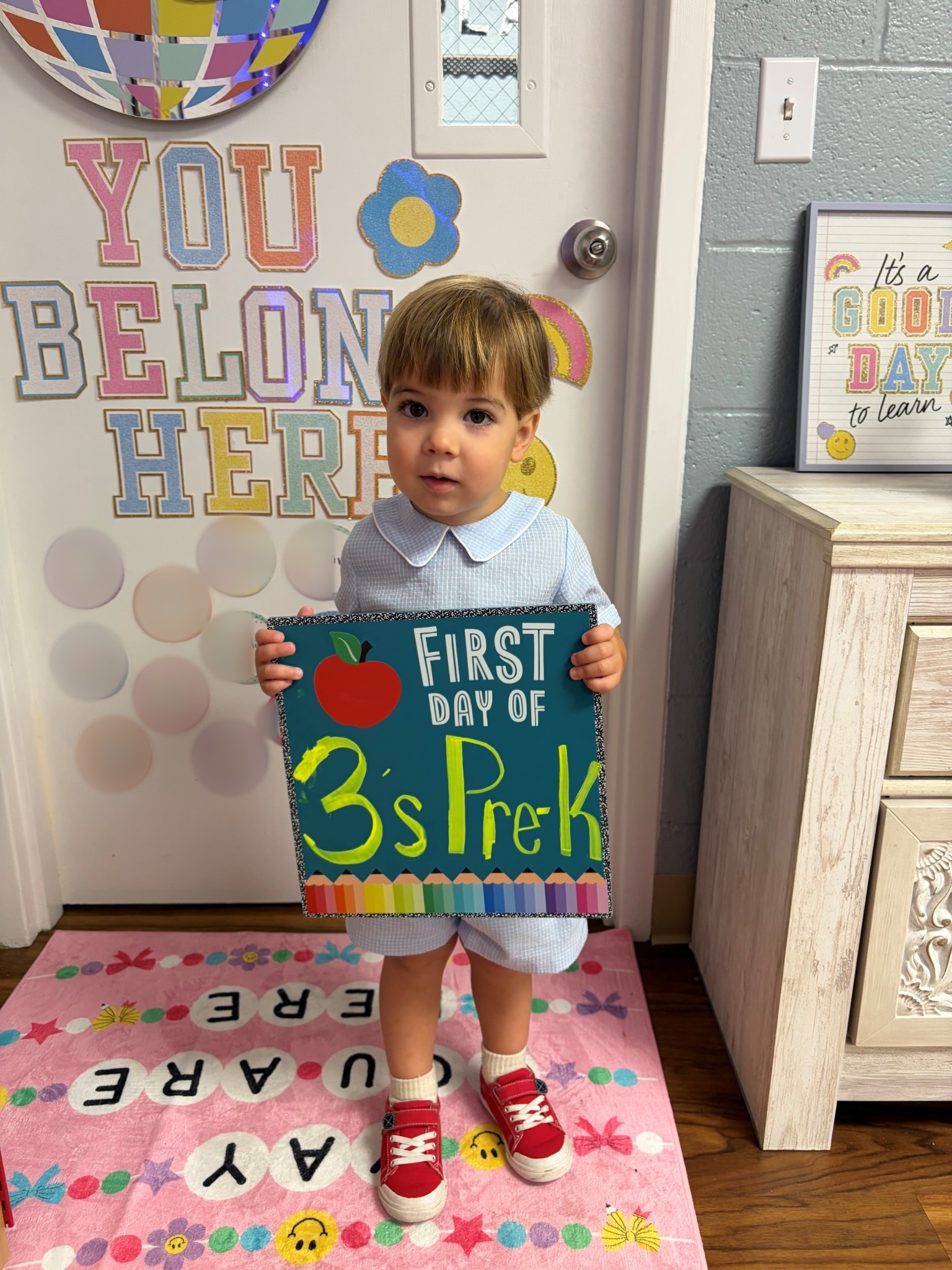 Preschooler holding a First Day of 3s Pre-K sign